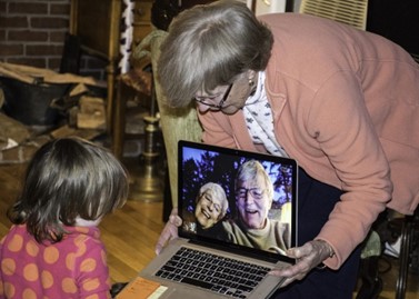 Nainen näyttää lapselle tietokoneelta isovanhemmat, jotka hymyilevät.